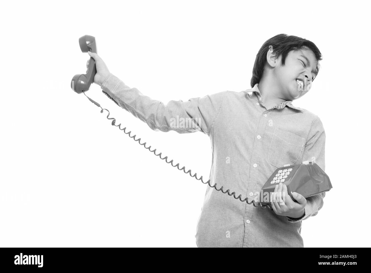 Studio shot of cute Japanese boy holding old telephone away looking irritated Stock Photo