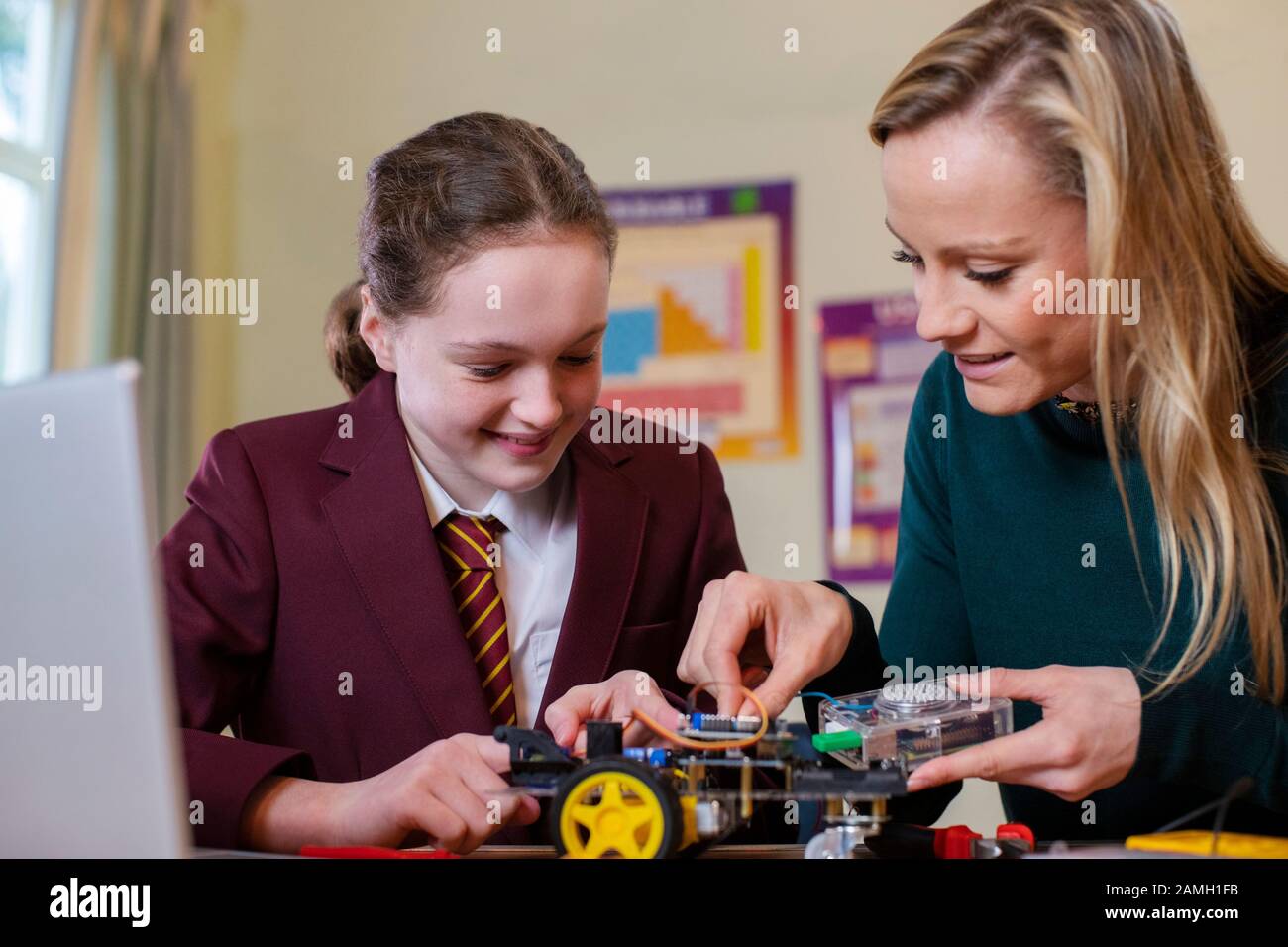 Teacher Helping Female Pupil Wearing Uniform To Build Robot Car In Science Lesson Stock Photo