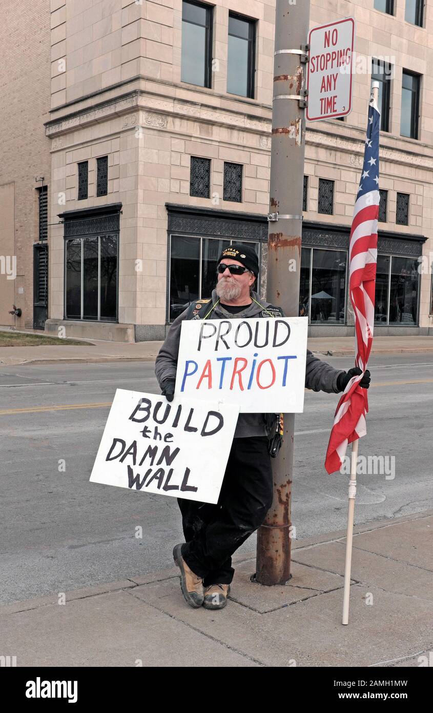 A Trump supporter stands with signs stating 'Proud Patriot' and 'Build the Damn Wall' on a street in Toledo, Ohio, USA during a Trump political rally. Stock Photo