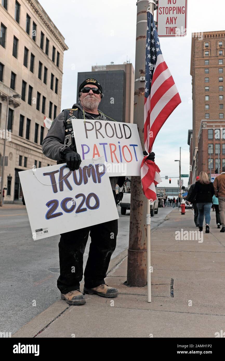 A self-declared proud American patriot holds an American flag along with signs stating 'Trump 2020' and 'Proud Patriot' in Toledo, Ohio, USA. Stock Photo