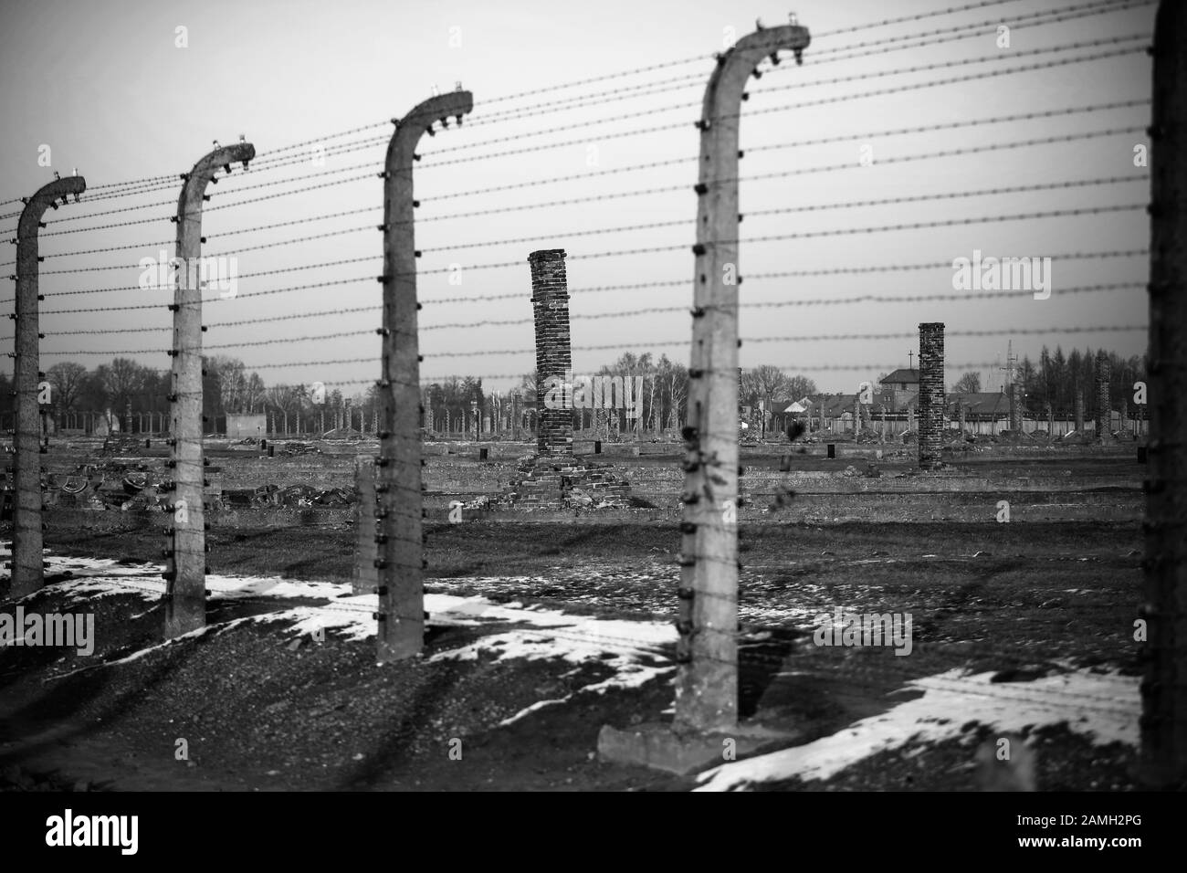 Auschwitz- Birkenau, Poland - electric fence with barbed wire, destroyed barracks, gas chambers and brick crematorium chimneys in concentration camp Stock Photo