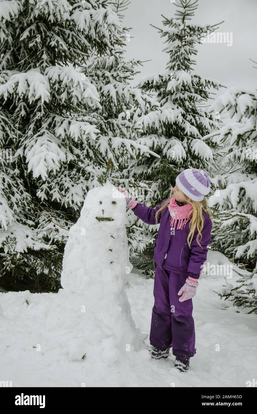 teen child having fun in happy winter forest white bulding a snowman statue Stock Photo