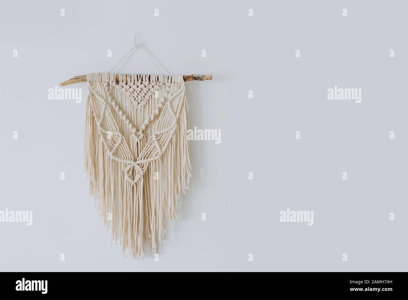 Handmade stylish cotton macrame decoration hanging on a white empty wall. Copy space. Stock Photo
