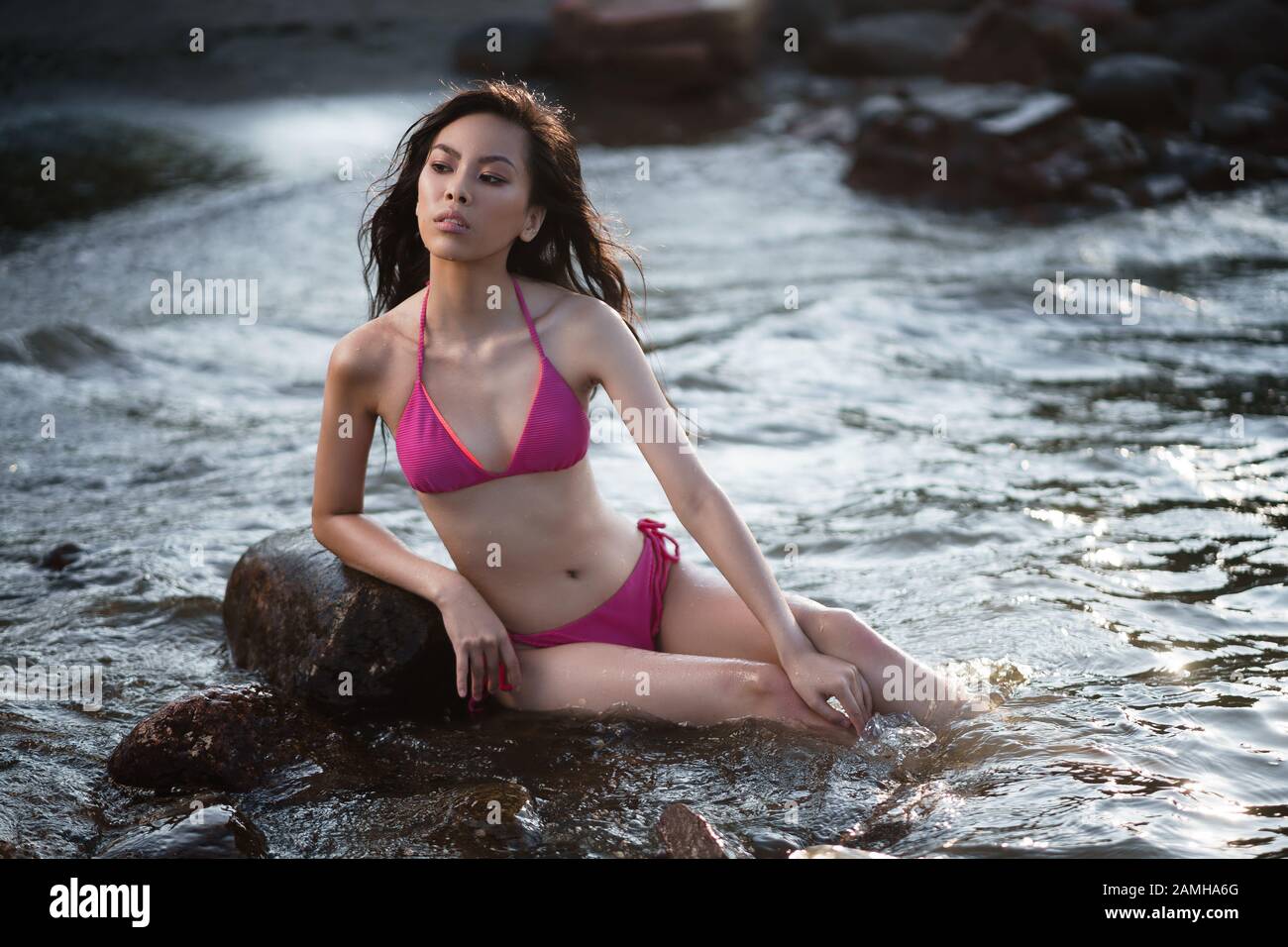 Concept: tourism, holidays, travel. Young lean pretty asian girl in two pieces pink swimsuit relax on seashore. Fashion photoshoot. Stock Photo