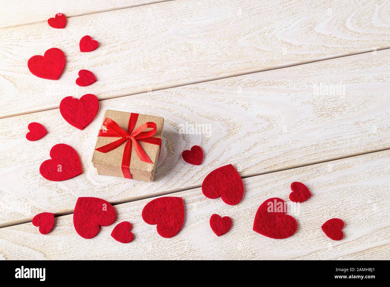 Craft paper gift box with red ribbon bow and scattering of valentine ...