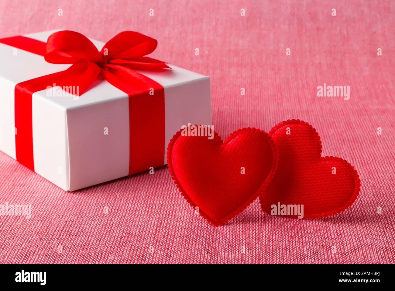 White gift box with red ribbon bow and two silk valentine hearts on a ...