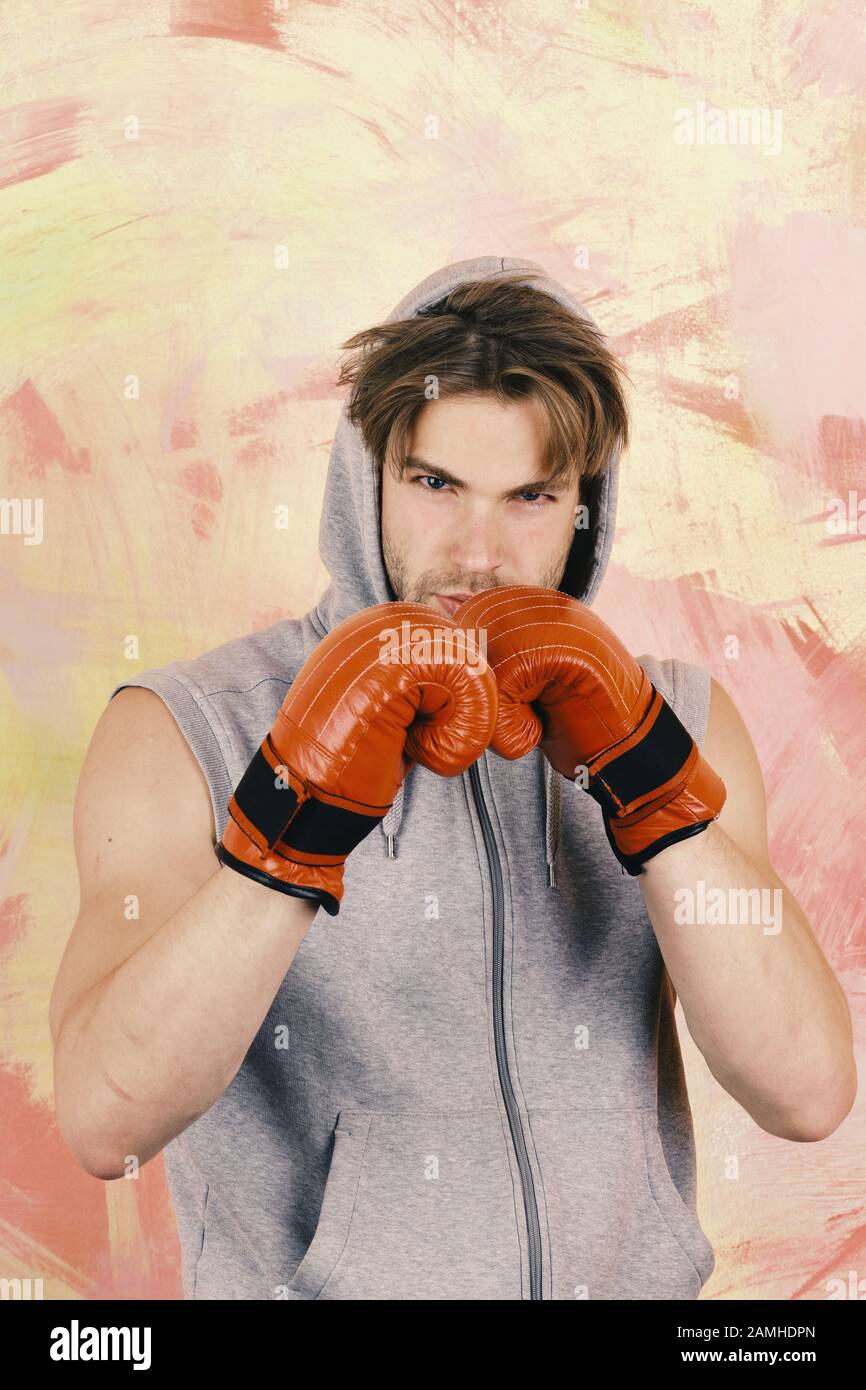Man with messy hair on colorful background. Sports and fight concept. Boxer with concentrated face trains to hit. Guy in grey sleeveless hoodie wears red leather boxing gloves Stock Photo