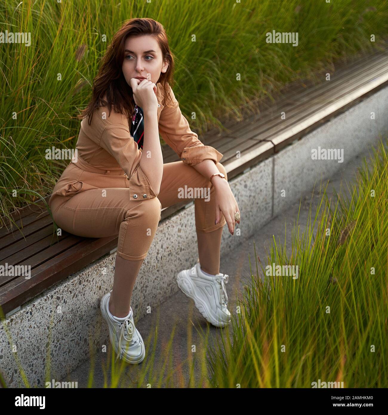 Young beautiful red haired gen z girl wearing slim fitted women beige khaki coverall overall denim jumpsuit or flight suit and white chunky platform Stock Photo