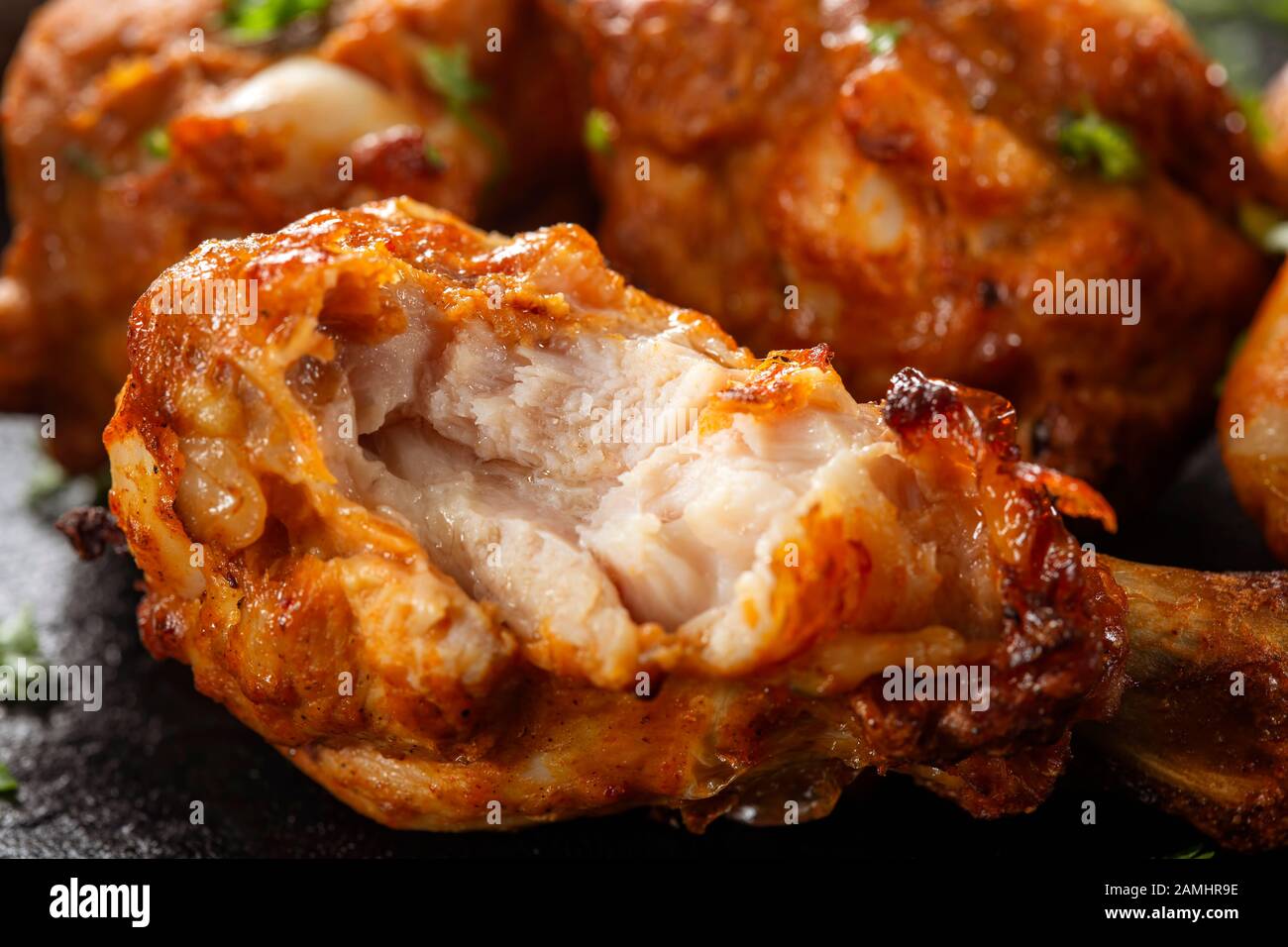 Bitten roasted chicken drumstick on dark slate - close up view Stock Photo