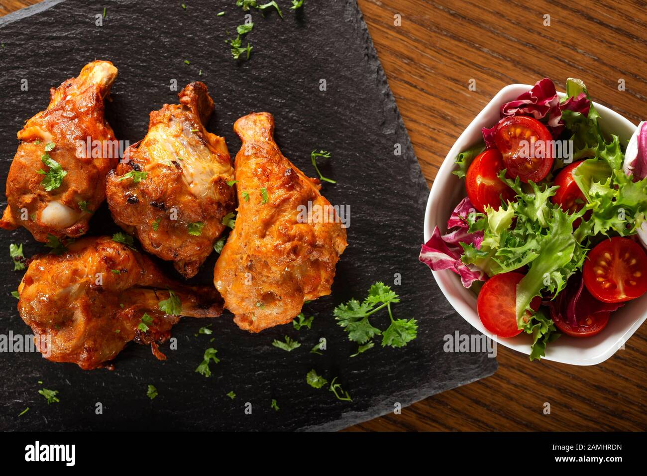 Roasted chicken drumsticks with salad on dark slate - top view Stock Photo