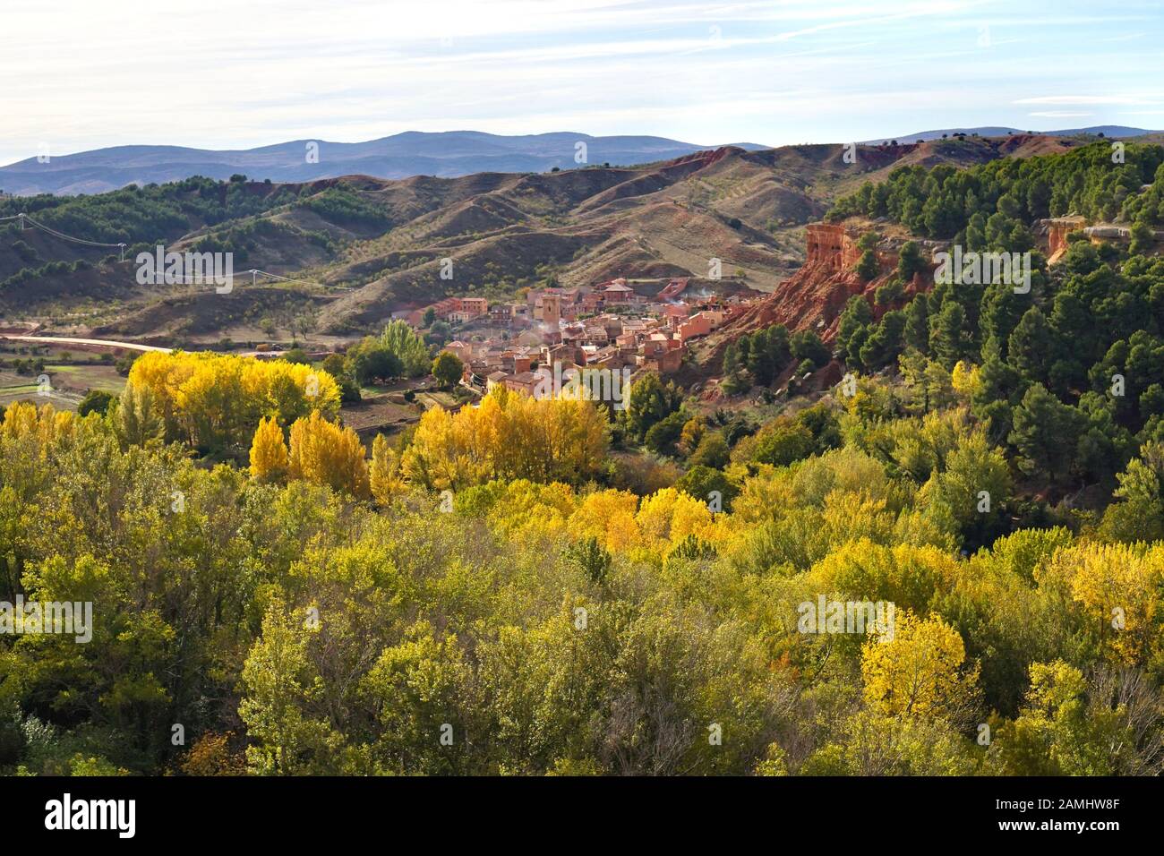 A view of a village built into the red rock surrounded by mountains & autumnal trees Stock Photo