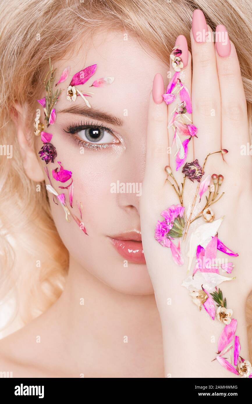 Cosmetics and manicure. Close-up portrait of attractive woman with dry flowers on her face, pastel color of nail design, perfect make-up and skin Stock Photo