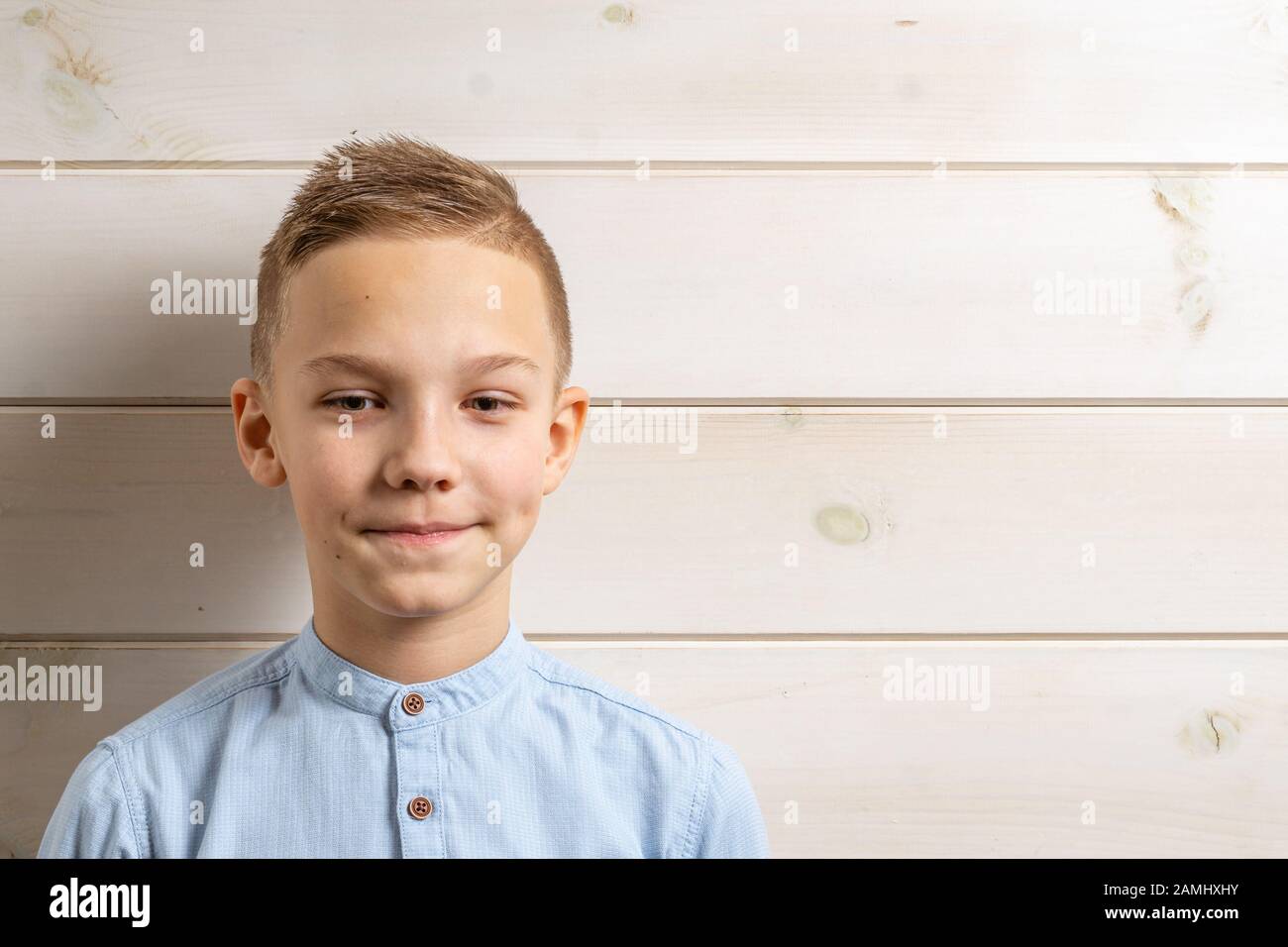 A boy of 10 years old in a blue shirt smiles on a light wooden ...