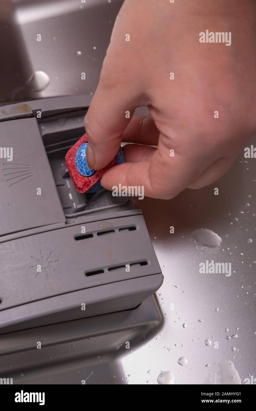 Installing detergent in the dishwasher. A female hand inserts a blue