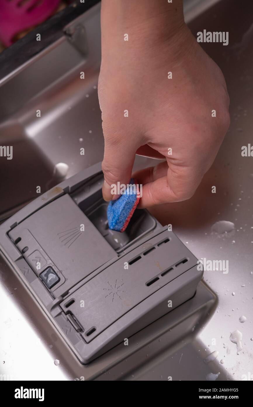 Installing detergent in the dishwasher. A female hand inserts a blue