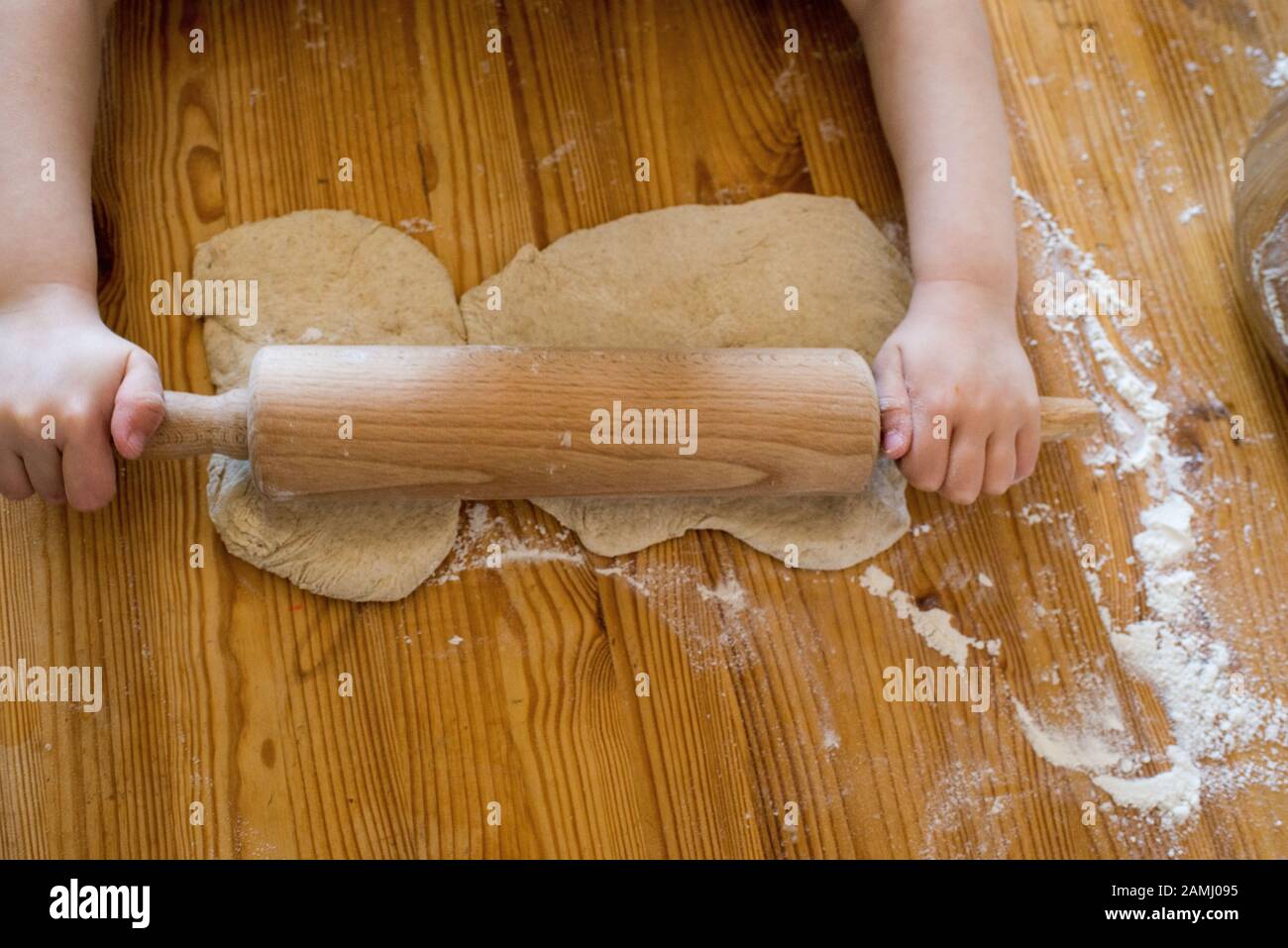 Hands of a boy rolling out dough on a wooden desk in a kitchen Stock Photo