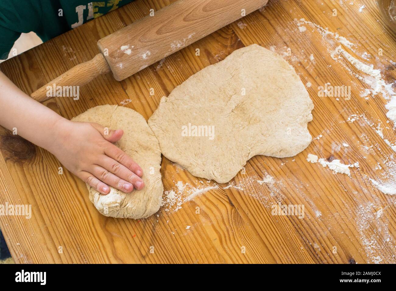Hands of a boy rolling out dough on a wooden desk in a kitchen Stock Photo