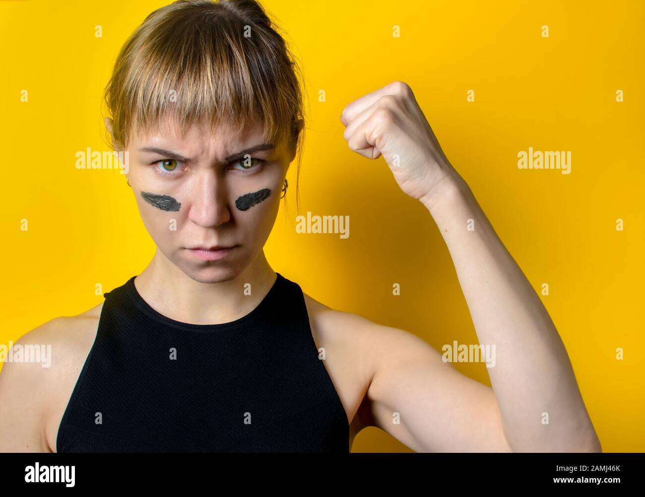 a woman with camouflage on her face on a yellow background shows a fist. feminism concept Stock Photo