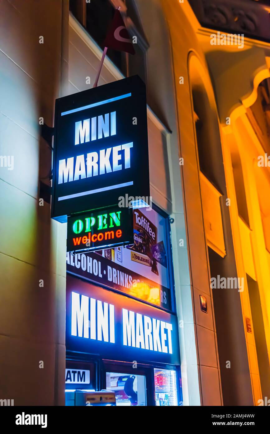 Sign outside a mini market at night, advertising food, alcohol, drinks, tobacco and essential items. Stock Photo