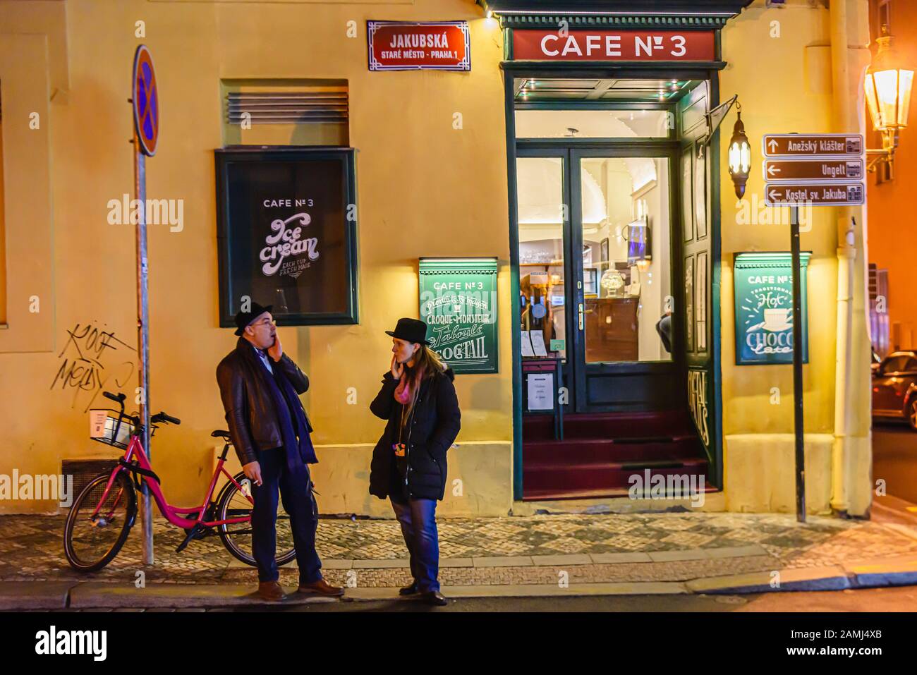 Two people standing outside a cafe at night while they have a cigarette, Prague, Czech Republic Stock Photo