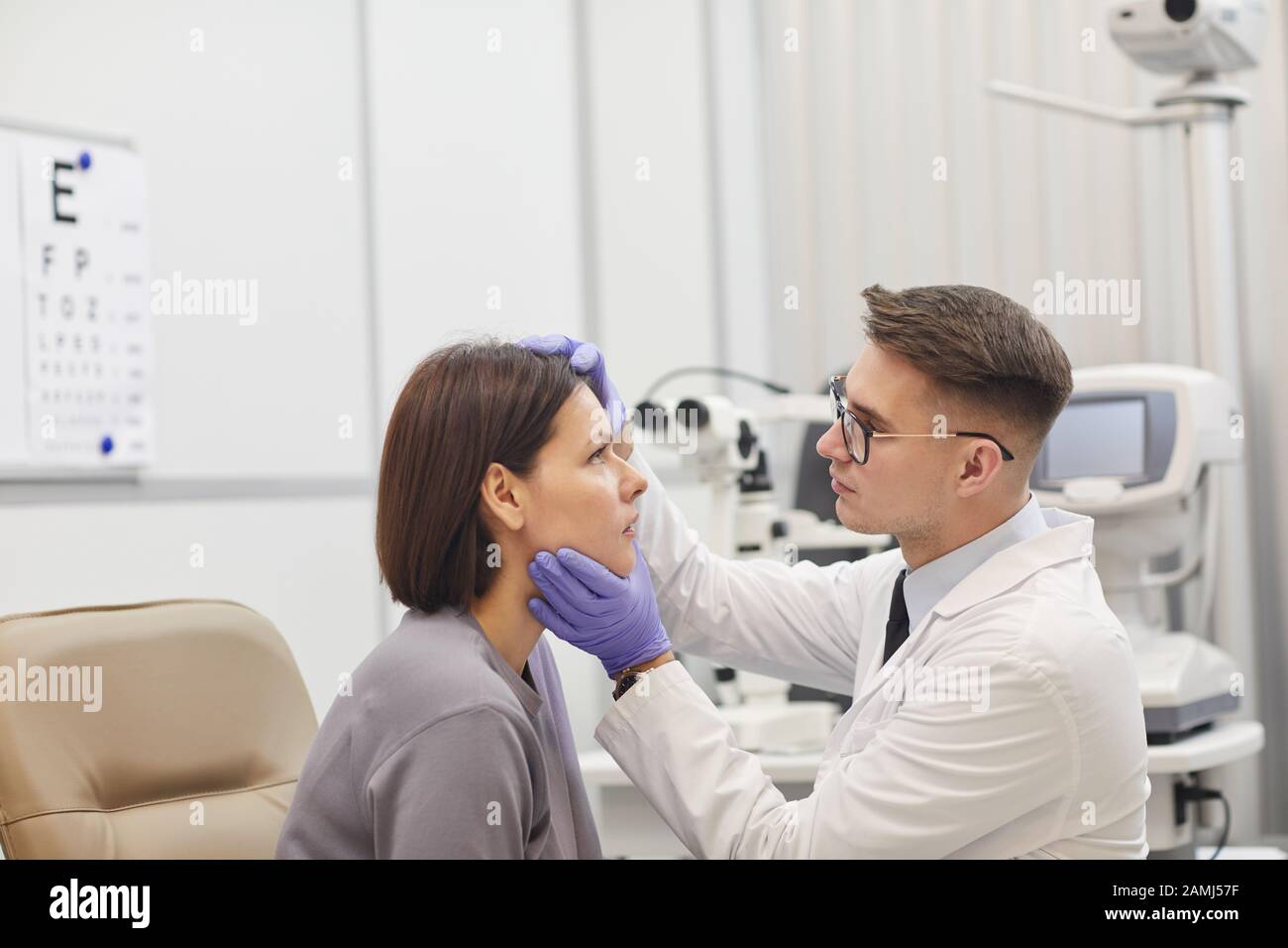 Side view portrait of young ophthalmologist opening eye of female patient while checking her vision in med clinic, copy space Stock Photo