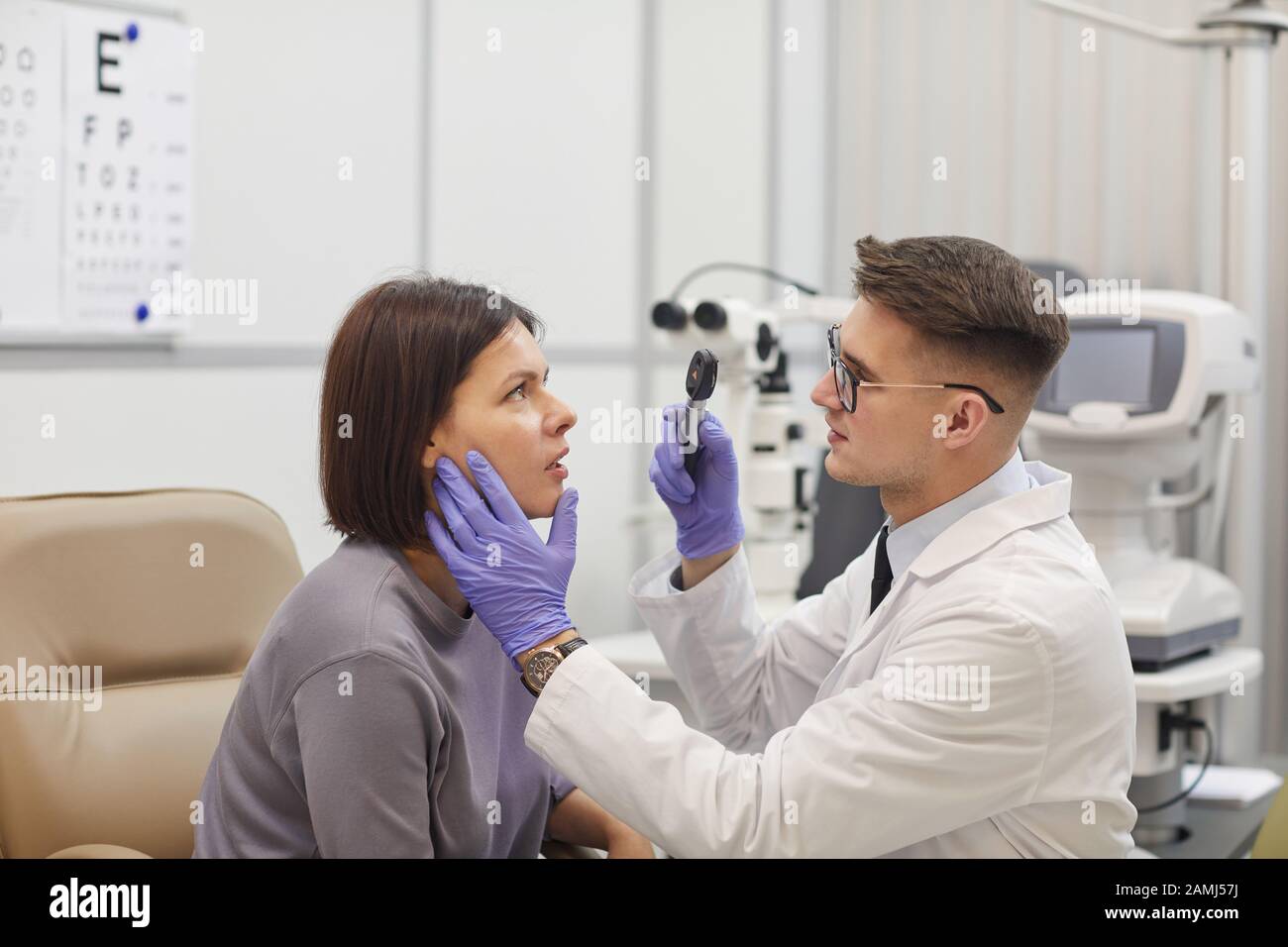 Side view portrait of young ophthalmologist checking eyesight of female patient during consultation in med clinic, copy space Stock Photo