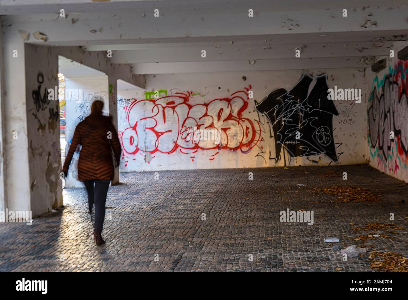 A lone woman walks through along an urban covered footpath with lots of graffiti. Stock Photo