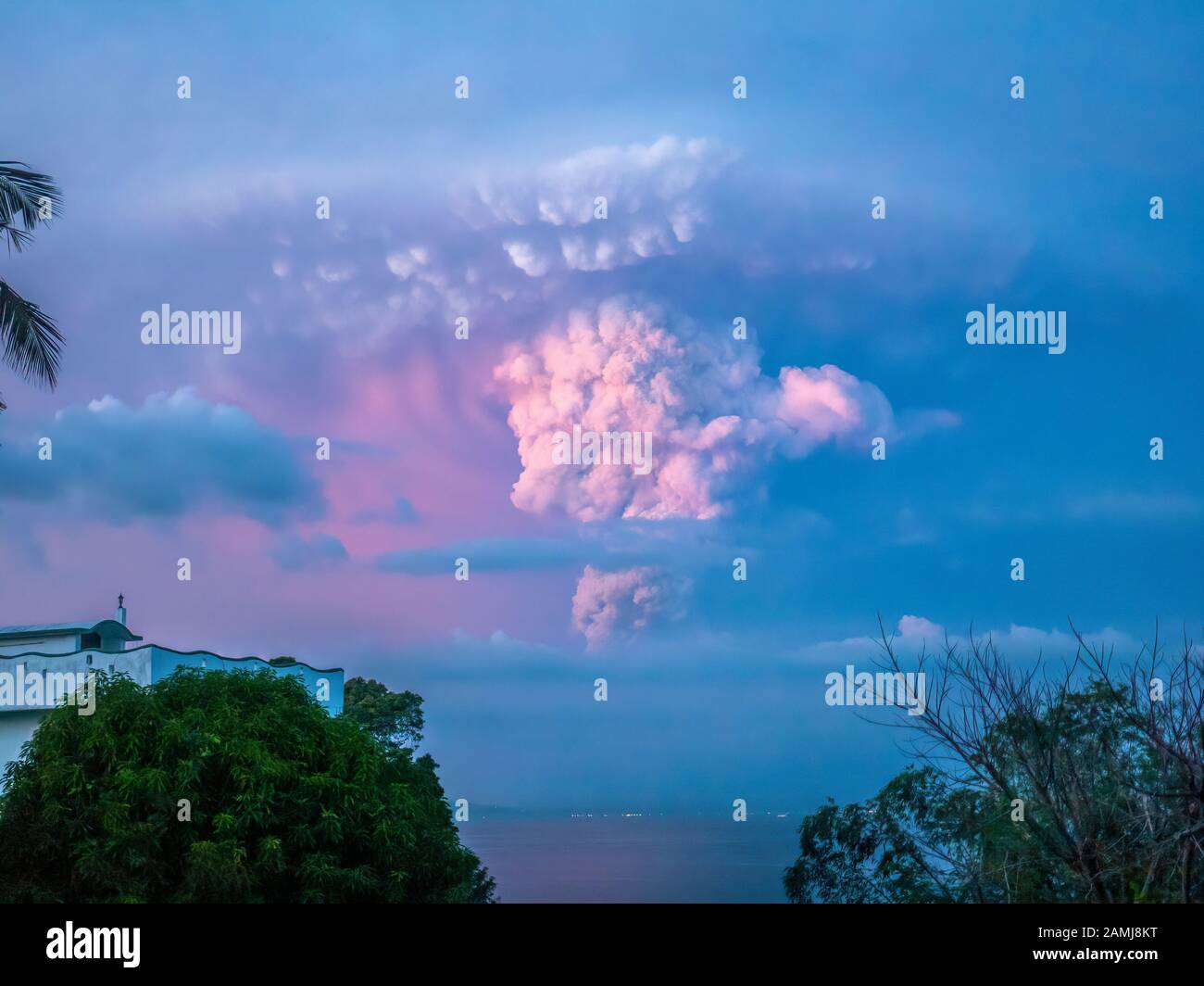 Taal Volcano eruption at sunset, Jan 12, 2020, its plume visible in the sky over the lights of Batangas City, viewed from Mindoro Is, 30 miles away. Stock Photo