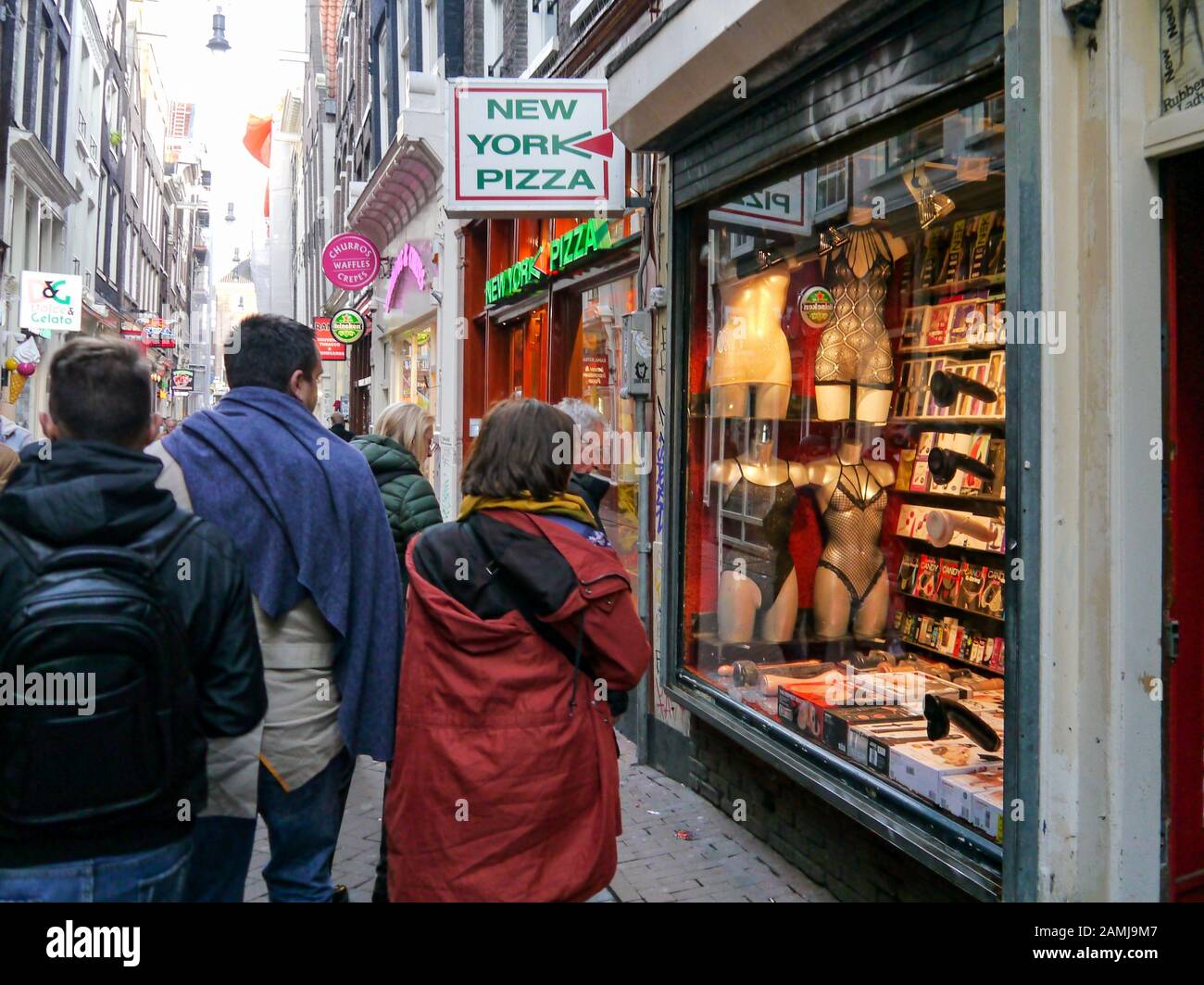 Tourists on an Amsterdam side street walk past an adult sex shop window Stock Photo