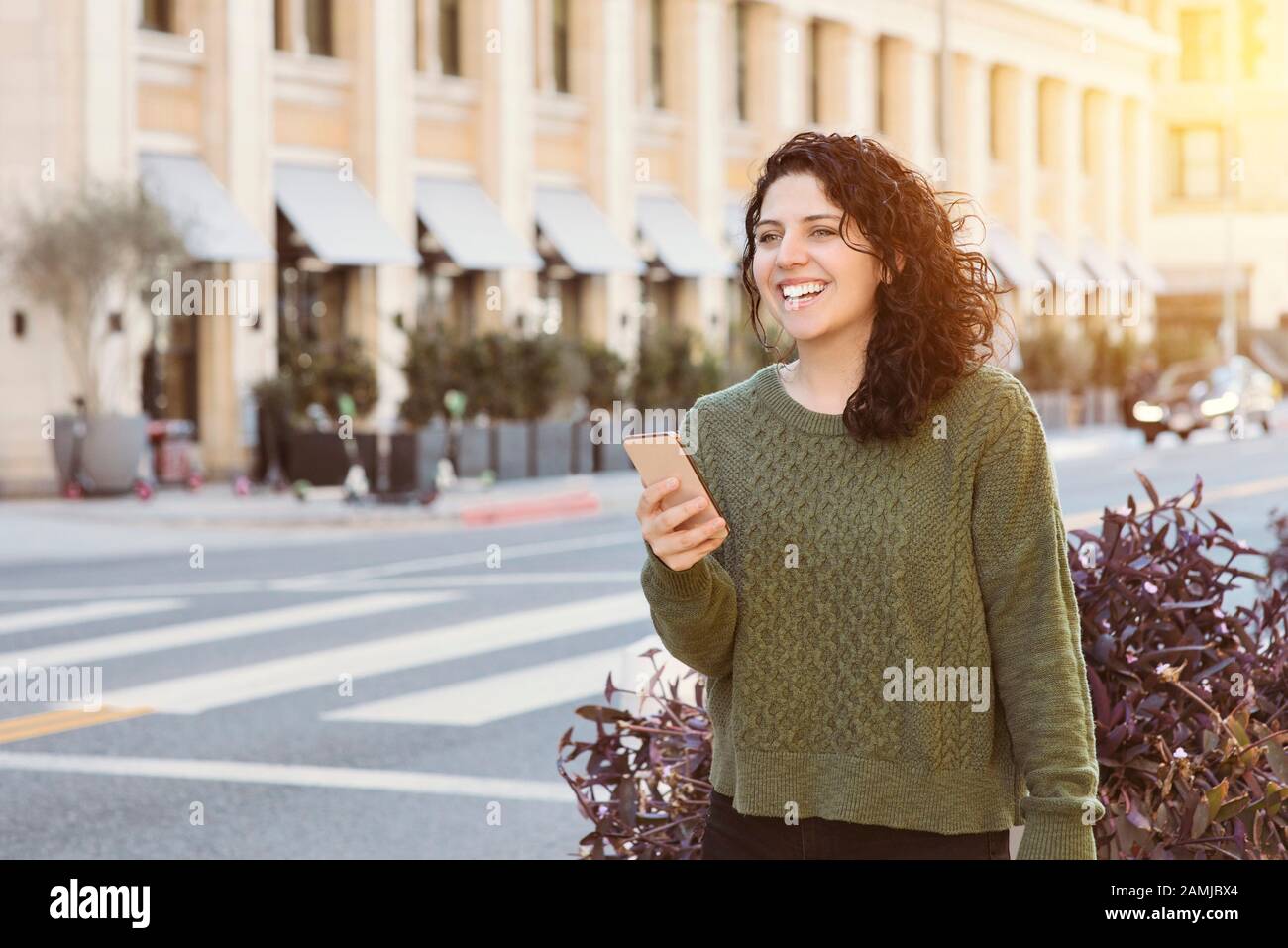 Caucasian woman holds her cell phone while waiting for ab uber in the City - Warm light in the daytime - Concept happy using technology Stock Photo