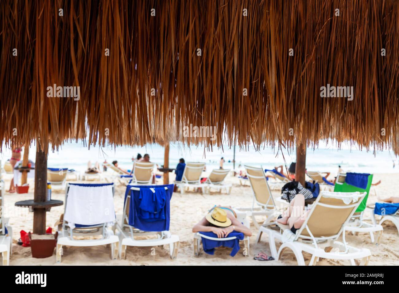 Close up of coconut palm leaf beach umbrella with beachgoers relaxing at a distance in a Cancun beach in Mexico. Stock Photo