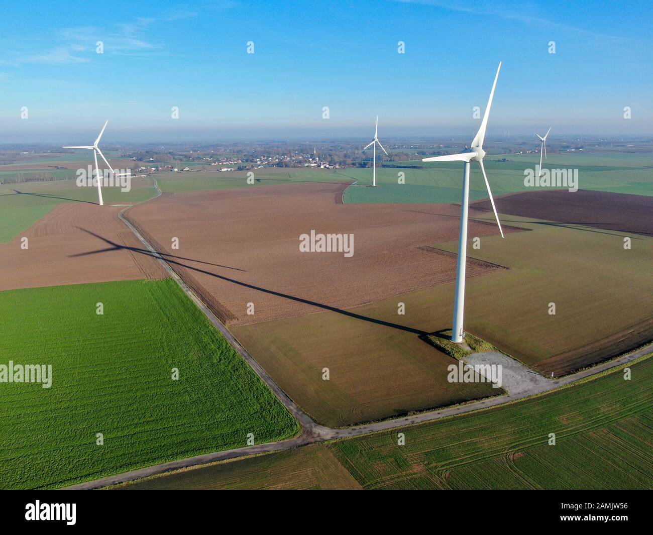 Aerial view of wind turbines on agricultural fields during blue winter day. Energy production with clean and renewable energy. Stock Photo