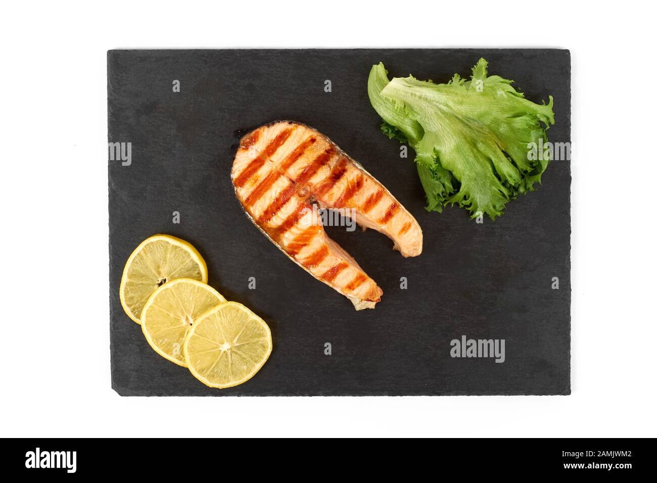 Roasted salmon steak with lemon and salad on slate. Isolated on white background Stock Photo