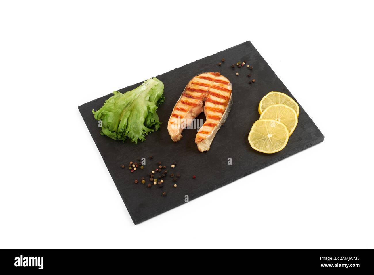 Roasted salmon steak with lemon and salad on slate. Isolated on white background Stock Photo
