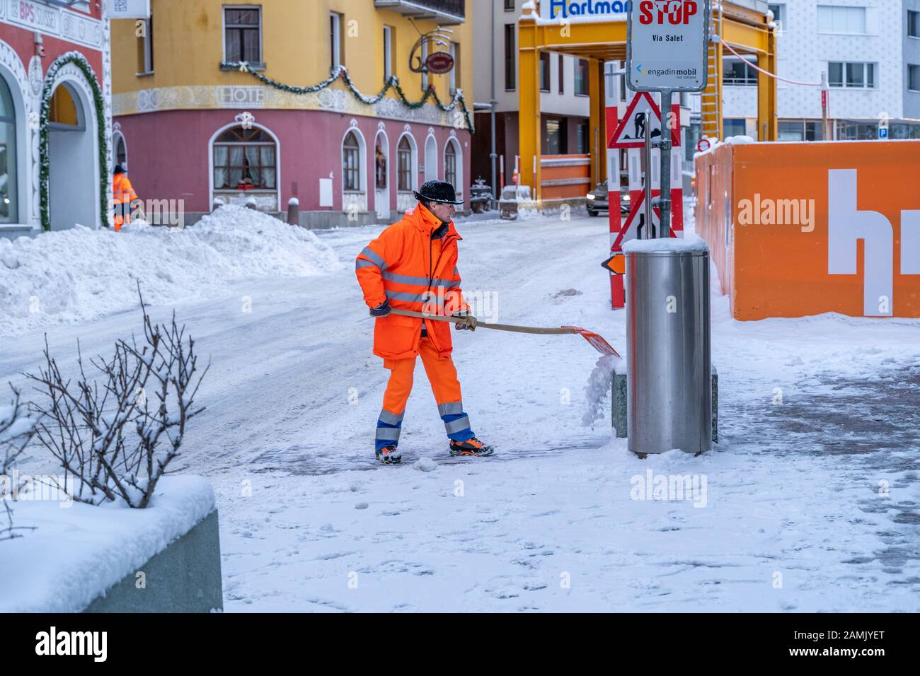 St. Moritz, Switzerland - 22 December - Road cleanup worker in bright orange coat clears up snow from the road at a street in St. Moritz, Switzerland Stock Photo