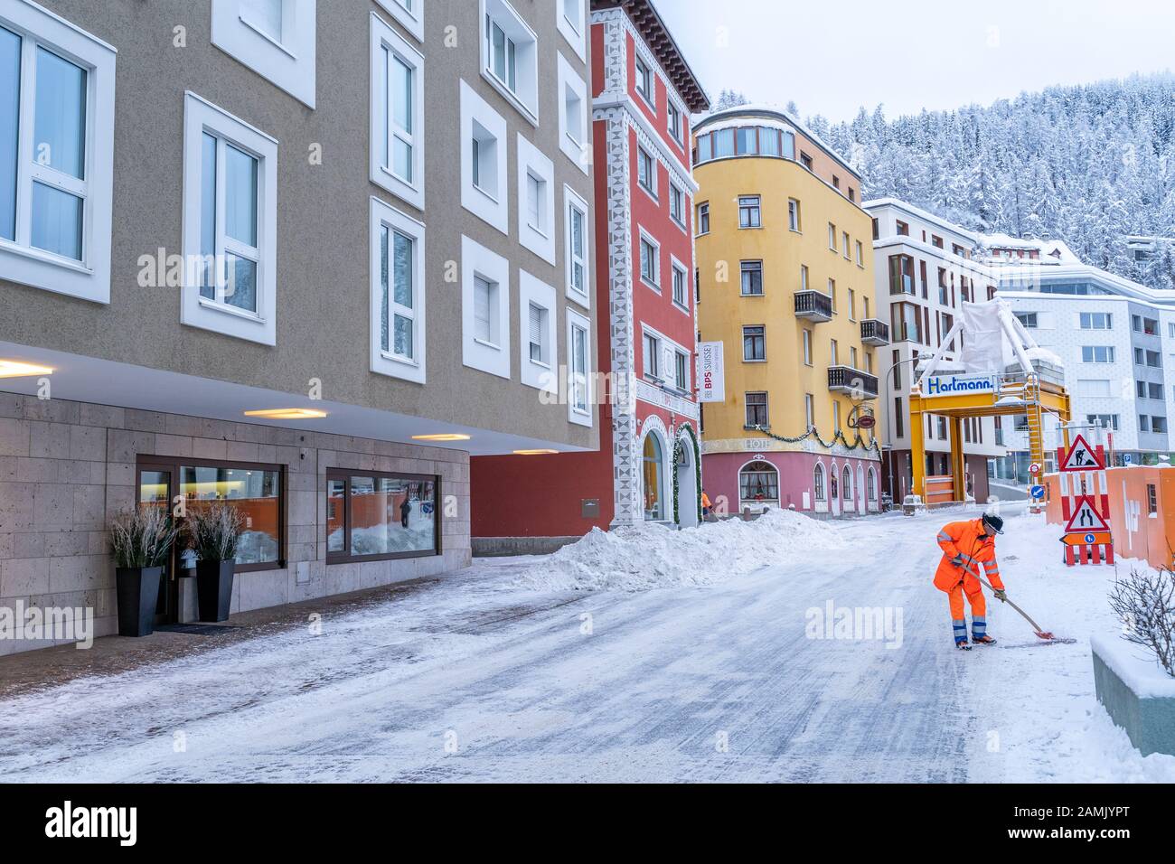 St. Moritz, Switzerland - 22 December - Road cleanup worker in bright orange coat clears up snow from the road at a street in St. Moritz, Switzerland Stock Photo
