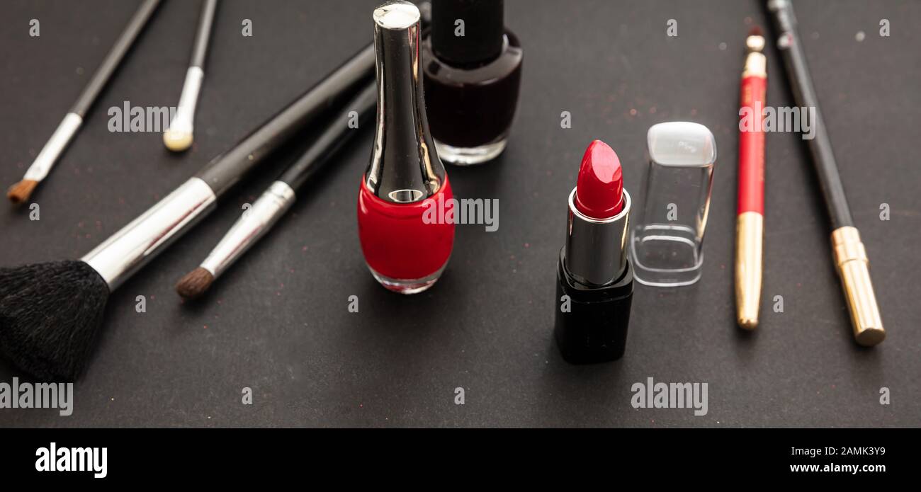 Make up cosmetics products in red and black. Red lipstick and nail polish, eye pencil and brushes against black color background Stock Photo