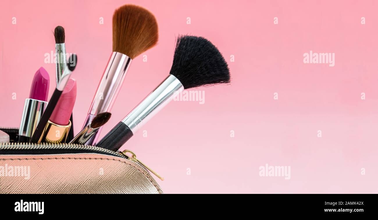 Make up cosmetic bag with professional accessories. Lipsticks and brushes in a gold cosmetic bag against pink color background, close up view, copy sp Stock Photo