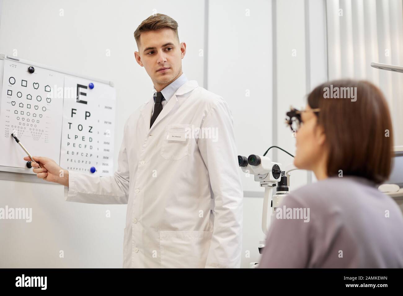 Portrait of young optometrist pointing at vision chart while checking eyesight of female patient in modern ophthalmology clinic Stock Photo