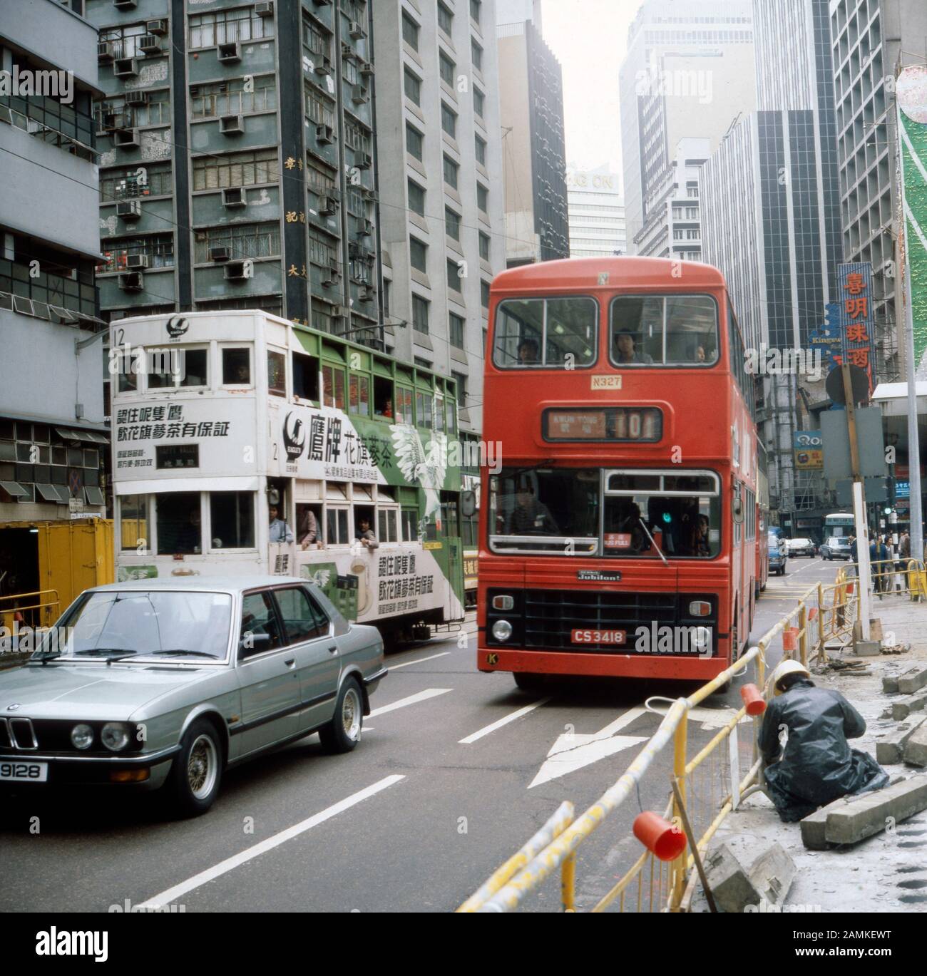Doppelstöckiger Bus nebem Straßenbahn mit Werbung in Hongkong, 1980er Jahre. Double decker bus and tram with advertisement in the streets of Hong Kong, 1980s. Stock Photo