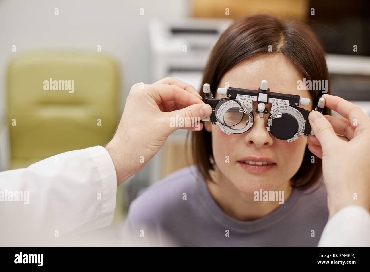Closeup of unrecognizable ophthalmologist putting trial frame on female patient during vision check in modern clinic, copy space Stock Photo
