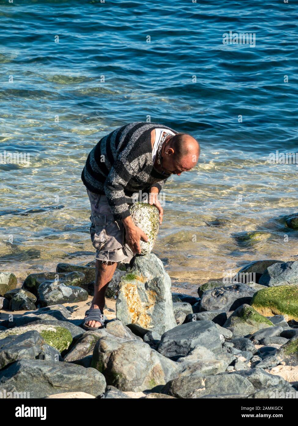 Balanced rock artist creating balanced stone sculptures our of beach pebbles on St Ives, Cornwall, England, UK Stock Photo