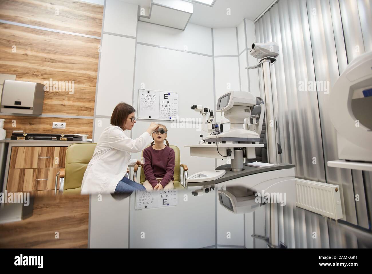 Wide angle portrait of cute teenage girl wearing trial frame during childs vision test in modern ophthalmology clinic, copy space Stock Photo