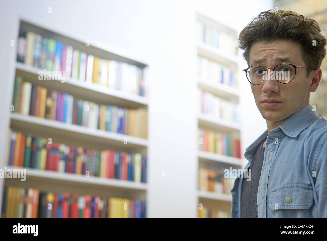 Young student with glasses, looking helpless and overcharged into the camera in library at university. Stock Photo