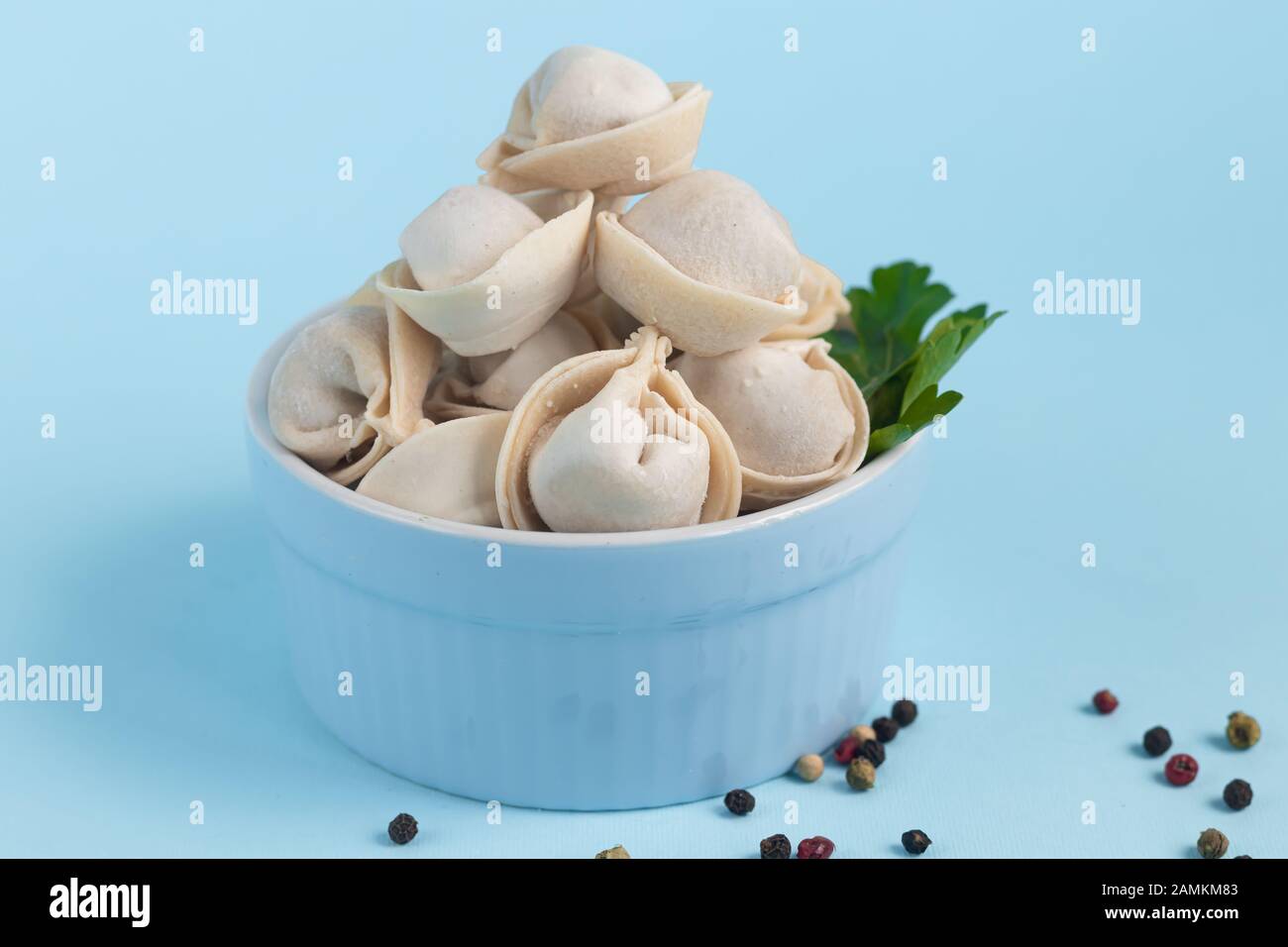 Raw, frozen dumplings in a blue bowl on a light background. With