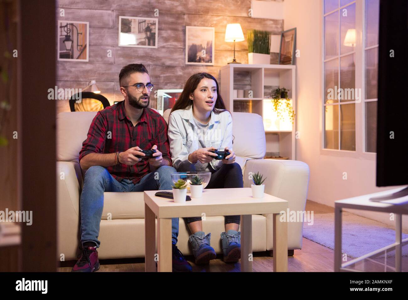 Young couple having a good time while playing video games on television. Couple sitting on sofa. Stock Photo
