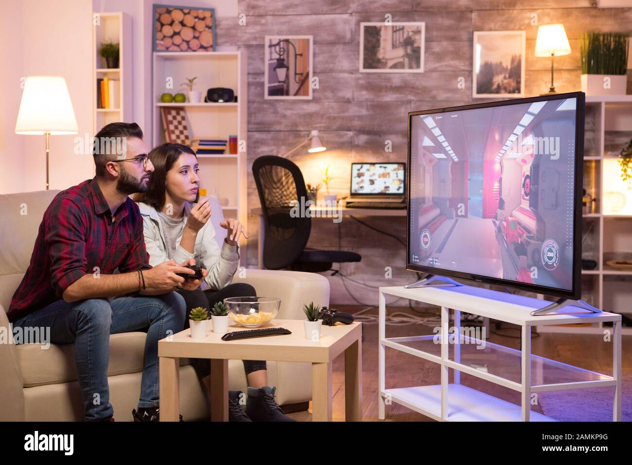Man sitting on couch and playing video games on television while his girlfriend is eating chips. Stock Photo