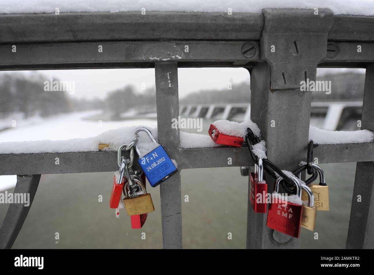 Padlocks as a declaration of love on the snow-covered bridge railing of the cable bridge. In the background the jetty. [automated translation] Stock Photo