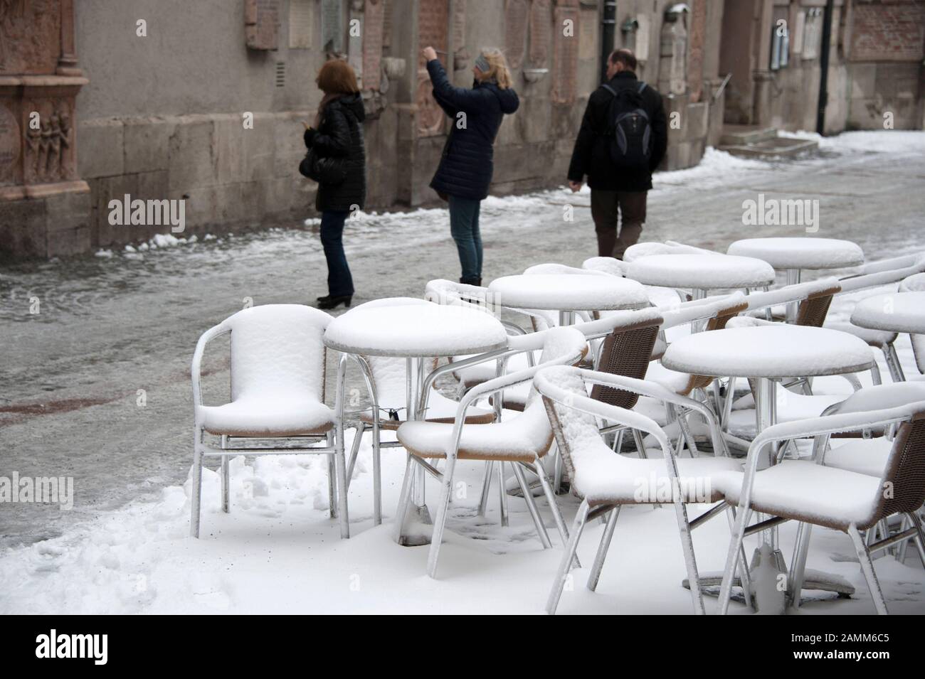 Thickly snowed-in furniture of a street cafe at Alter Peter on a cold March day. Tourists taking pictures in the background. [automated translation] Stock Photo