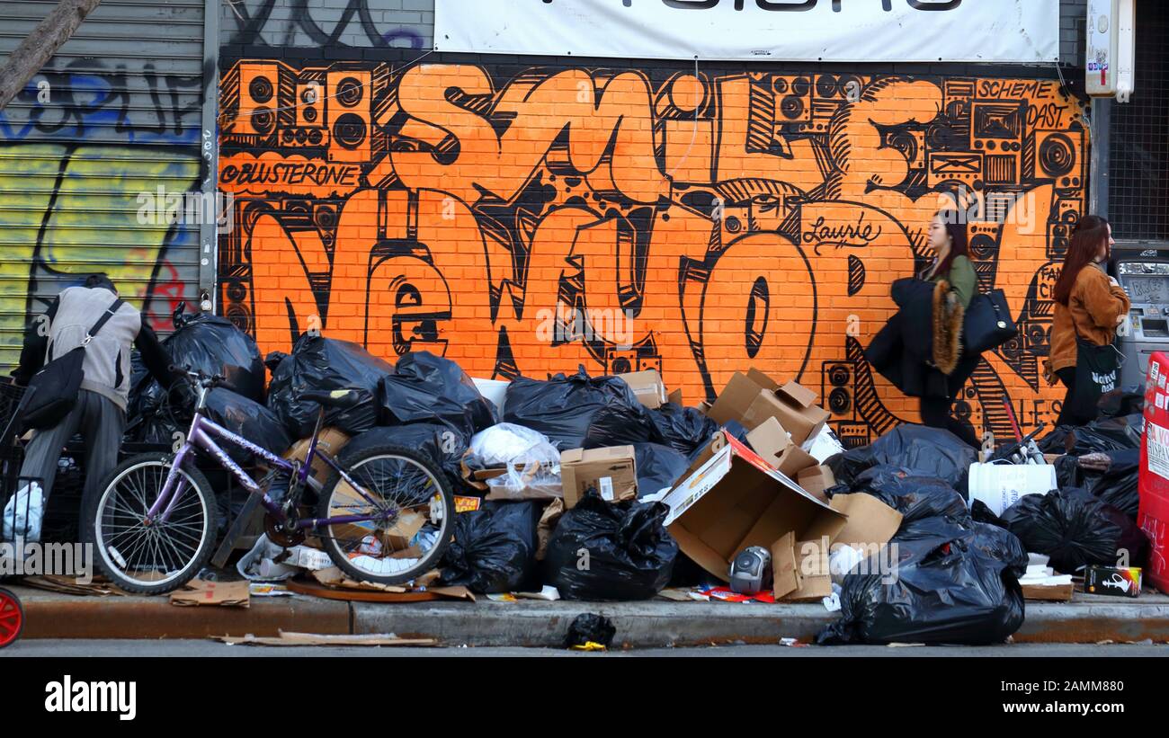 People walk past a pile of garbage on a New York City sidewalk with graffiti in the background and somebody rummaging through trash, January 12, 2020. Stock Photo